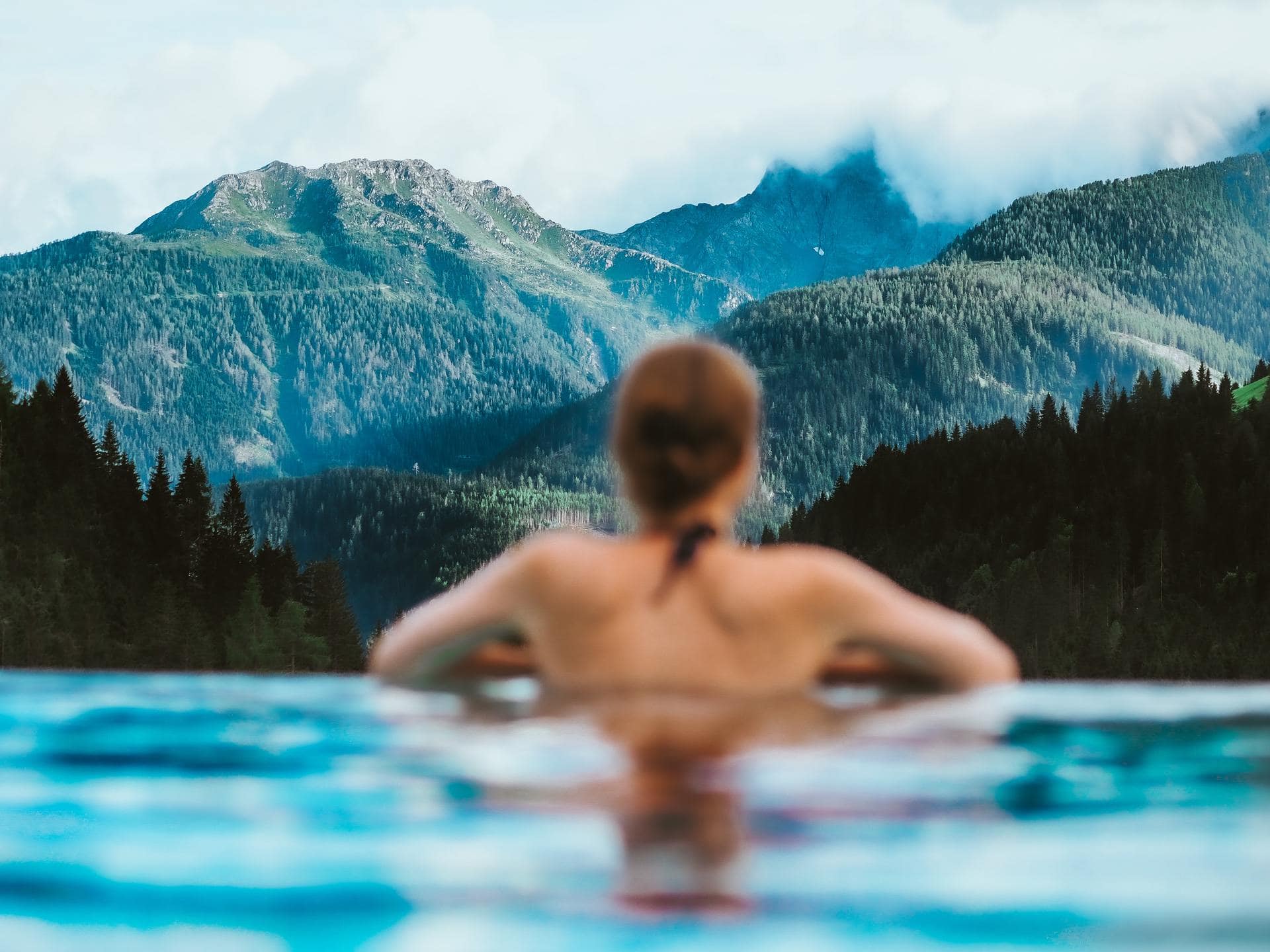 Woman in a resort swimming pool looking at a mountain view.